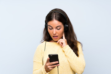 Young woman listening music with a mobile over isolated blue wall