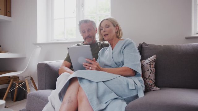 Senior Couple Sitting On Sofa At Home Using Digital Tablet Together