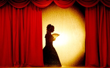 A man and woman in theatrical costumes in the theater of shadows on the stage with red curtains....