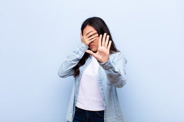young latin pretty woman covering face with hand and putting other hand up front to stop camera,...