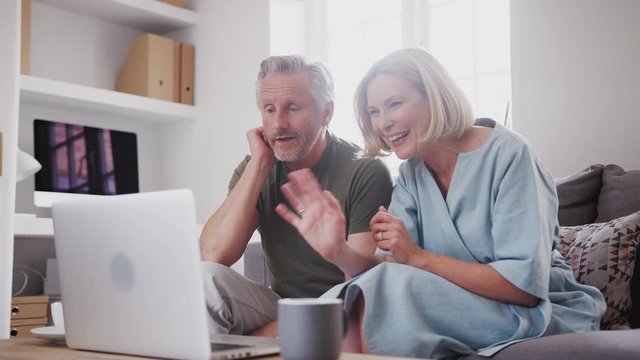 Senior Couple Sitting On Sofa At Home Making Video Call Using Laptop Computer Together