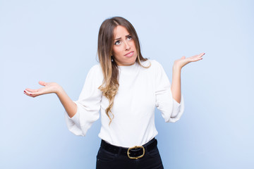 young pretty hispanic woman shrugging with a dumb, crazy, confused, puzzled expression, feeling...