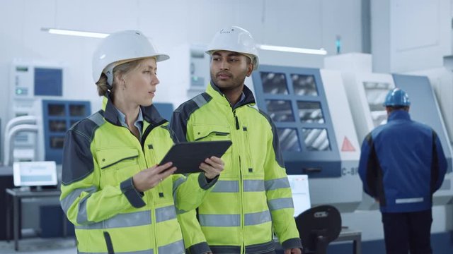 Chief Engineer and Project Supervisor in Safety Vests and Hard Hats Walk Through Modern Factory, Talking, Optimizing Production. Industrial Facility: Professionals Use Machinery. Following Front Shot