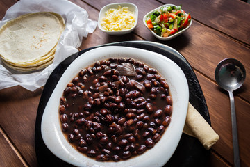 Plato de frijoles cocidos con tortillas y salsa mexicana quesillo en mesa de madera