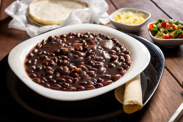 Plato de frijoles cocidos con tortillas y salsa mexicana quesillo en mesa de madera