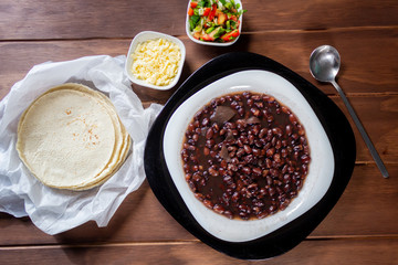 Plato de frijoles negros con salsa mexicana tortillas y queso cotija en mesa de madera