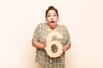 young pretty woman surprised, shocked, amazed, holding a number 6.
