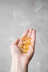 Female hand holds capsules of dietary supplements Omega-3 on a light background.