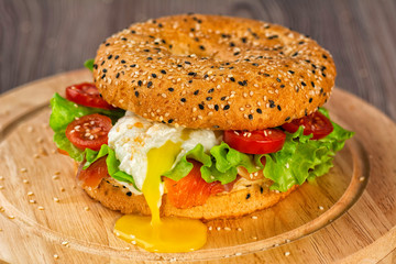 Fresh healthy bagel with salmon, lettuce, tomatoes and soft egg on a round board on a wooden kitchen table