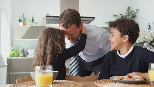 Daughter Helping Businessman Father To Put On Tie As Children Eat Breakfast In Kitchen Before School