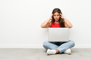 Young woman with a laptop sitting on the floor unhappy and frustrated with something. Negative facial expression