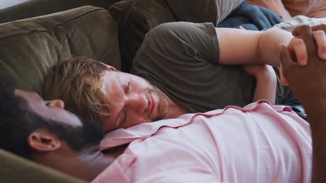 Loving Male Gay Couple Relaxing Lying On Sofa At Home Hugging And Kissing 