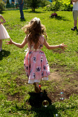 Little girl in a dress skipping runs on the green grass on a holiday.