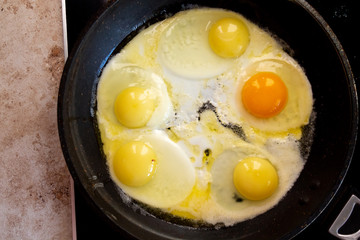 Bright orange egg yolk in a frying pan on a black skillet while preparing a family breakfast.