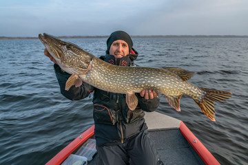 Happy fisherman with big pike fish. Boat fishing