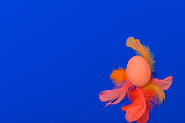 Obraz na płótnie Canvas Happy Easter flat lay of orange, red feathers and hand-painted eggs on a blue background. Easter minimal creative greeting card. Copy space.