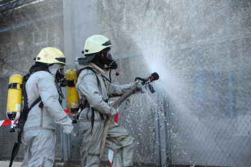Rescuers in protective rubber suits watering plant territory with syringe. Rescue team training in decontamination