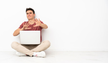 Teenager man sitting on the flor with his laptop nervous stretching hands to the front
