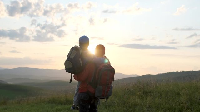 Happy family outdoors trip. Father and son traveling. Little boy child hiker tourist traveler backpacks walking on sunset mountain, hiking vacation travel tourism adventure summer nature. 4 K slow-mo
