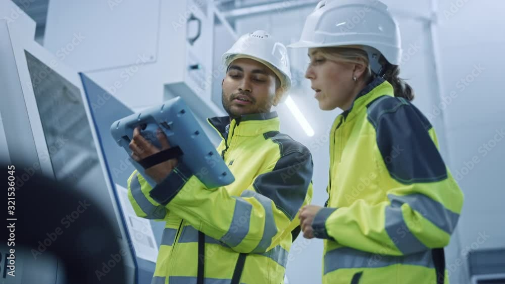 Poster Chief Engineer and Project Manager Wearing Safety Vests and Hard Hats, Use Digital Tablet Controller in Modern Factory, Talking, Programming Machine For Productivity. Low Angle Portraits