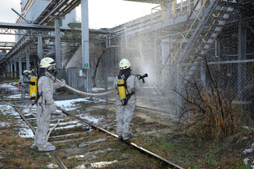 Rescuers in protective rubber suits watering plant territory with syringe. Rescue team training in...