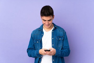 Teenager caucasian  handsome man isolated on purple background sending a message with the mobile