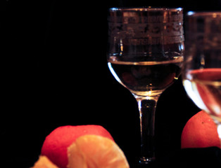 two glasses of champagne stand on a black background with tangerines. Bubbles of sparkling wine in a glass.