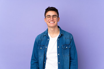 Teenager caucasian  handsome man isolated on purple background with glasses and happy