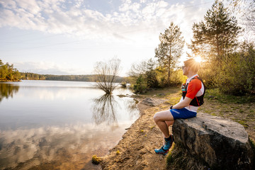 Sportive man sitting on a rock at the lakeside at sunset, Forstsee, Carinthia, Austria