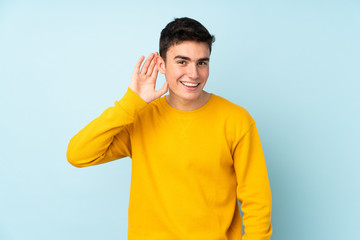 Teenager caucasian handsome man isolated on purple background listening to something by putting hand on the ear