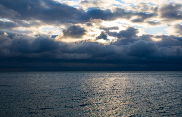 Fototapeta premium blue dark stormy clouds above the sea, the sunlight breaks through the clouds