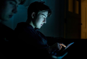 Two teenage boys using technology at home in the dark