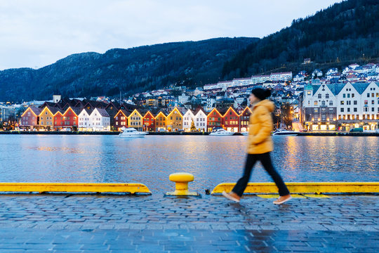 Woman wearing a yellow jacket and walking at harbor in Bergen, Norway