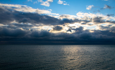 Fototapeta na wymiar blue dark stormy clouds above the sea, the sunlight breaks through the clouds