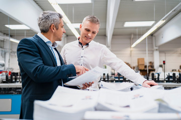 Two businessmen discussing paper in a factory
