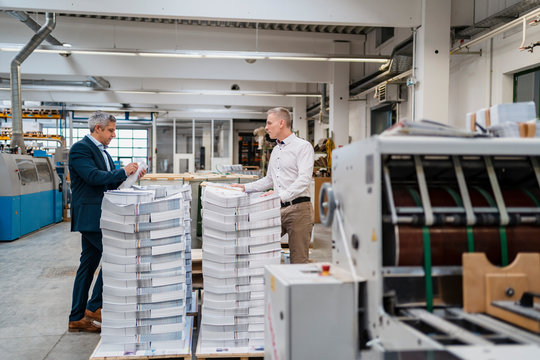 Two businessmen at stack of papers in a factory