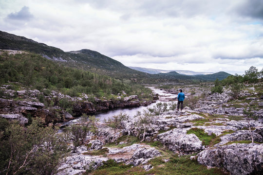 Man standing above river bank with mountains, Lakselv, Norway