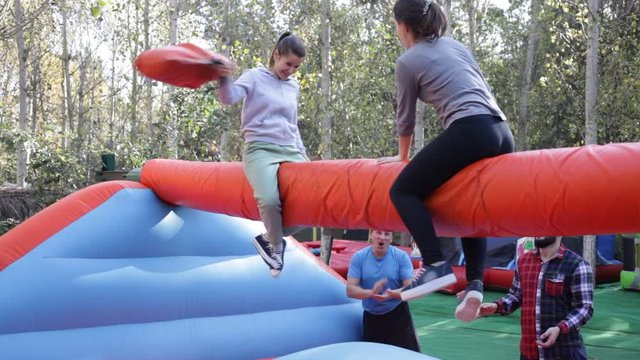 Two cheerful women having funny battle by big boxing gloves on inflatable arena at amusement park