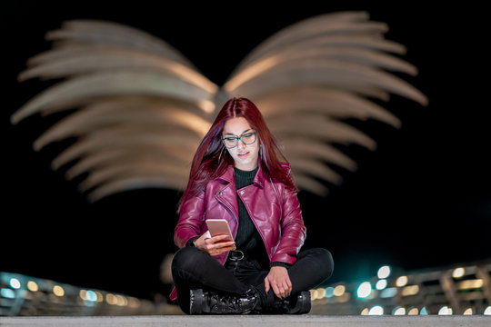 Portrait of teenage girl with red dyed hair looking at smartphone at night
