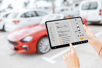 Woman controlling car with mobile application while standing near the vehicle outdoors, close-up...