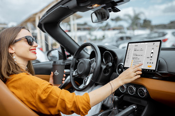 Cheerful woman controlling car with a digital dashboard, switching autopilot mode while driving a cabriolet. Smart car concept