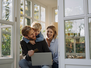 Family using laptop and credit card in sunroom at home