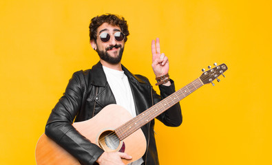 young musician man looking happy, confident and trustworthy, smiling and showing victory sign, with...