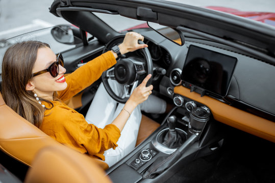 Young And Cheerful Woman Driving Sports Car With A Digital Touchscreen On The Front Dashboard