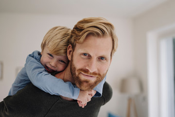 Portrait of smiling father carrying son piggyback at home