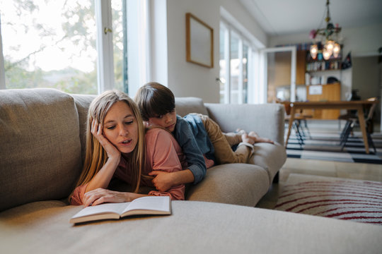 Mother and son lying on couch, using reading book