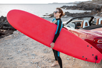 Portrait of a young woman surfer in swimsuit walking with surfboard on the rocky coast. Active...