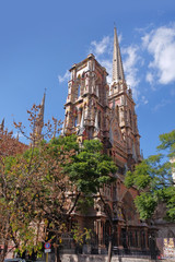 Vertical view of the Capuchins Church in Cordoba, Argentina, surrounded by green vegetation, against a blue sky covered by white clouds.