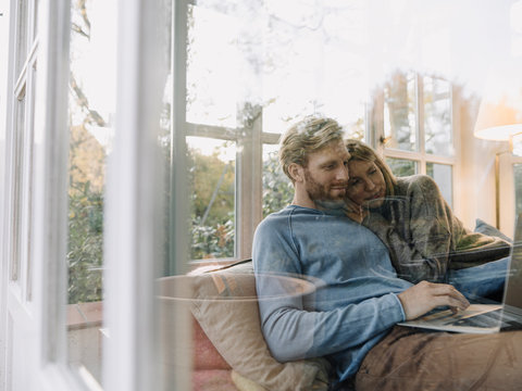 Man with wife using laptop in sunroom at home