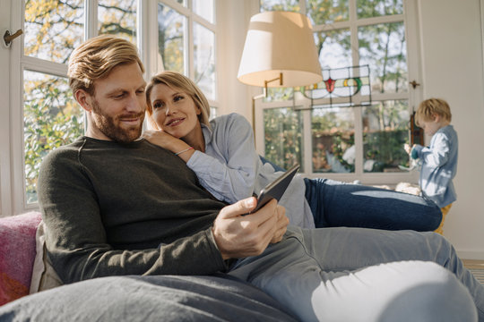 Couple using tablet in sunroom at home with son in background
